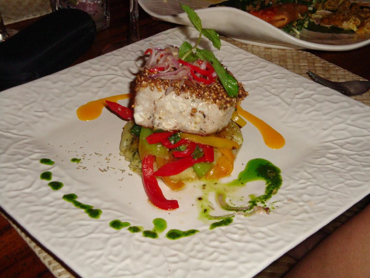 Un pavé de poisson en croûte de graines, sur des poivrons colorés, sauces vertes et orangées